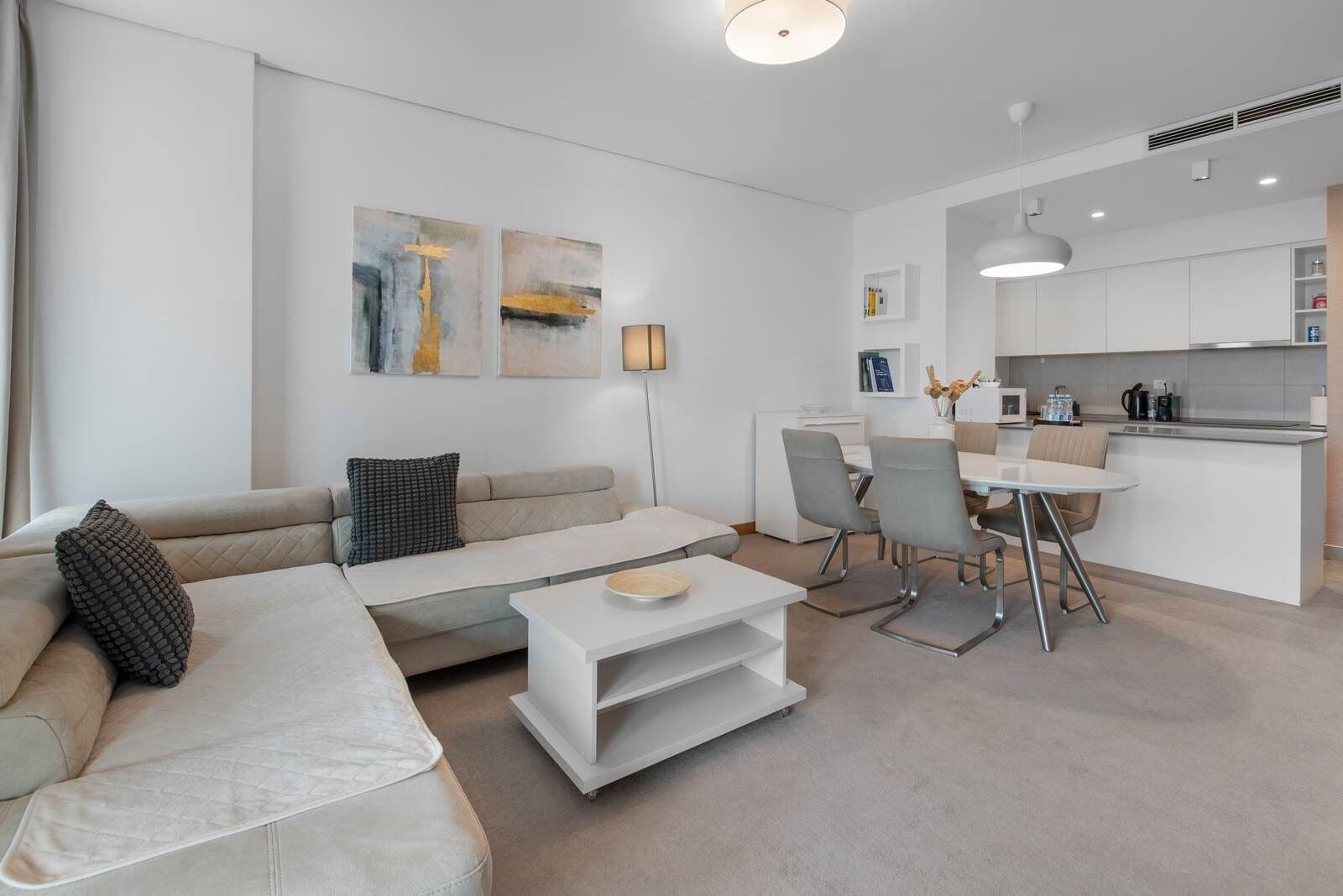 Un salon moderne comprenant un canapé, une table basse et un coin repas avec des chaises, ainsi qu’une petite cuisine.