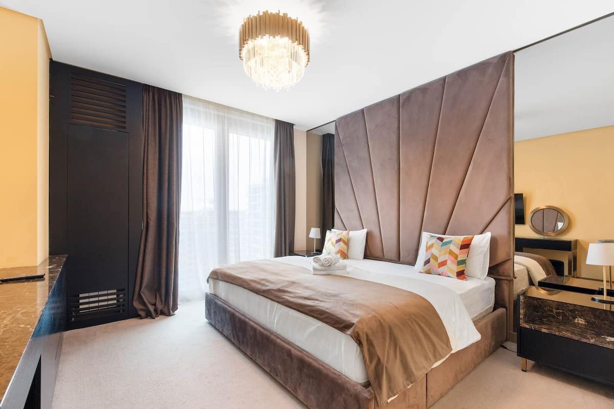 A hotel room with a large bed, a chandelier, a desk, and a window with curtains.