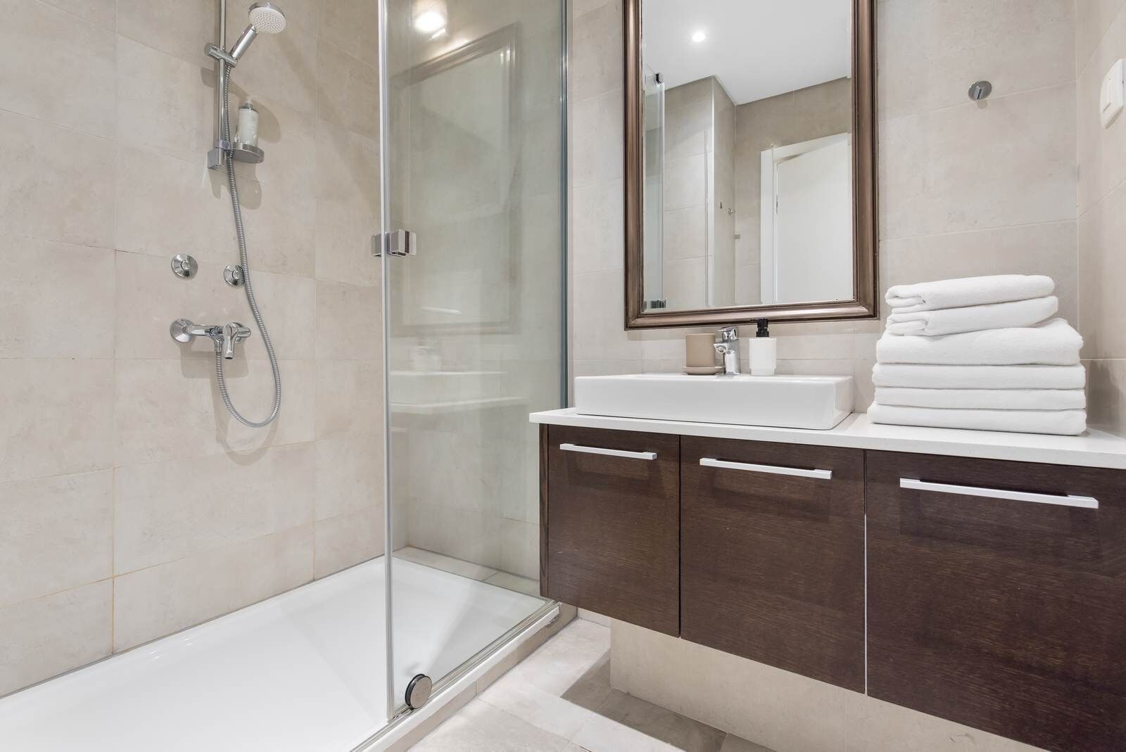 Un baño moderno con ducha envuelta en vidrio, una bañera blanca y un tocador con muebles de madera oscura.