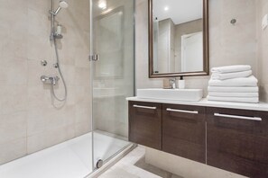A modern bathroom with a glass-enclosed shower, a white bathtub, and a vanity with dark wood cabinets. - Belgrade Waterfront Riverside Apartments (Belgrade)