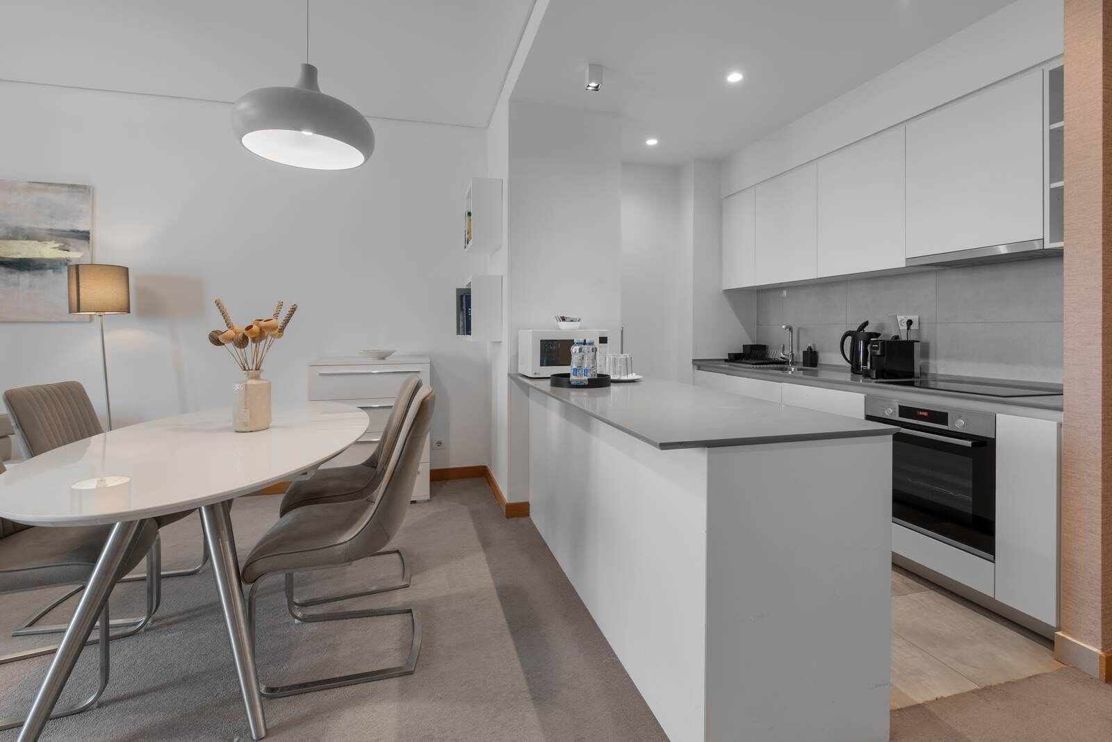 A modern kitchen with a dining area, white cabinetry, stainless steel appliances, and a pendant light.