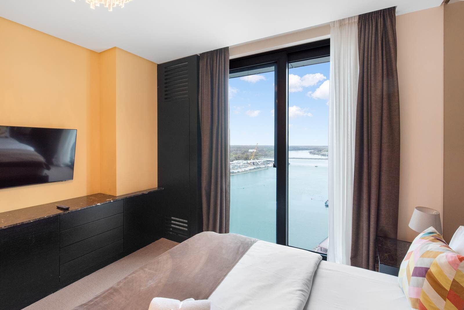 Ein Hotelzimmer mit Bett, Fernseher, Schreibtisch und Blick auf ein Gewässer.