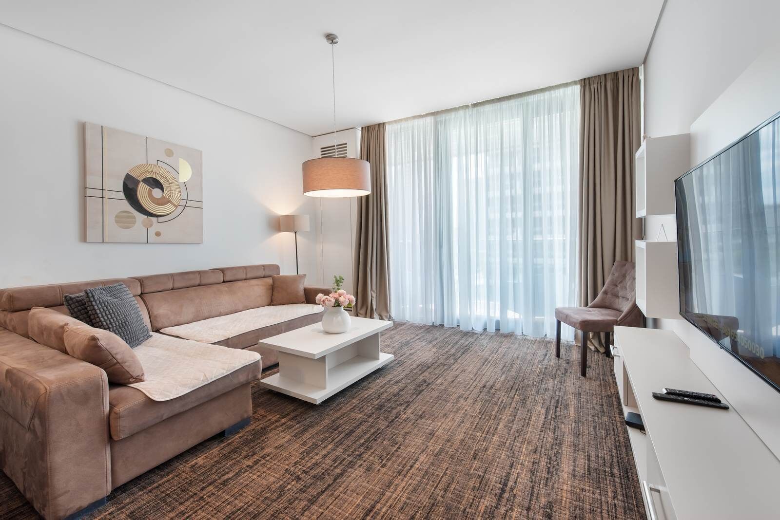 A modern hotel room with a sofa, coffee table, TV, and curtains.