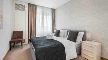 Una camera d'albergo con un letto, una sedia, un comodino e una finestra con tende.