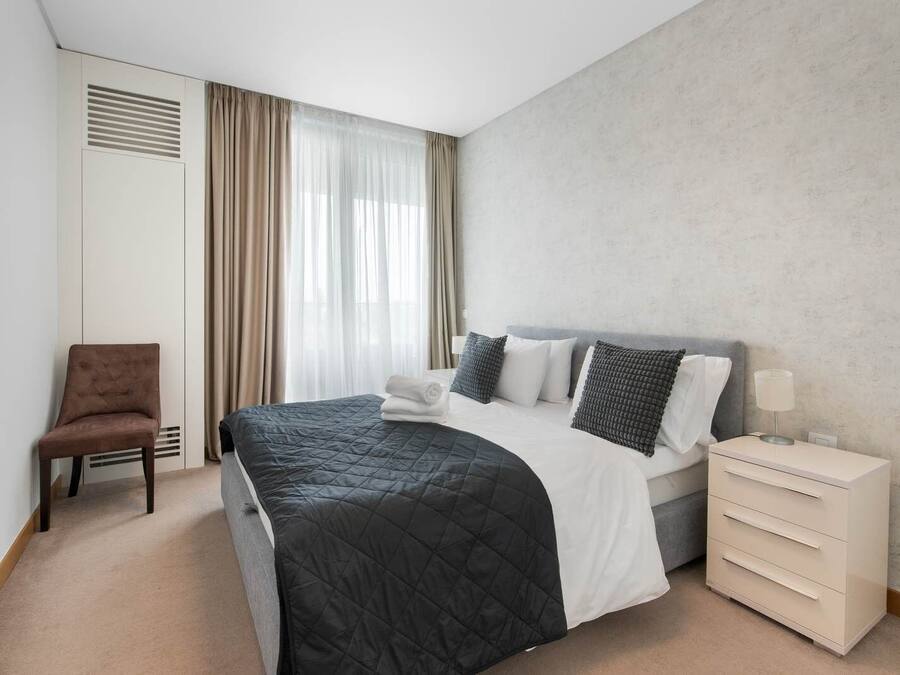 Una camera d'albergo con un letto, una sedia, un comodino e una finestra con tende.