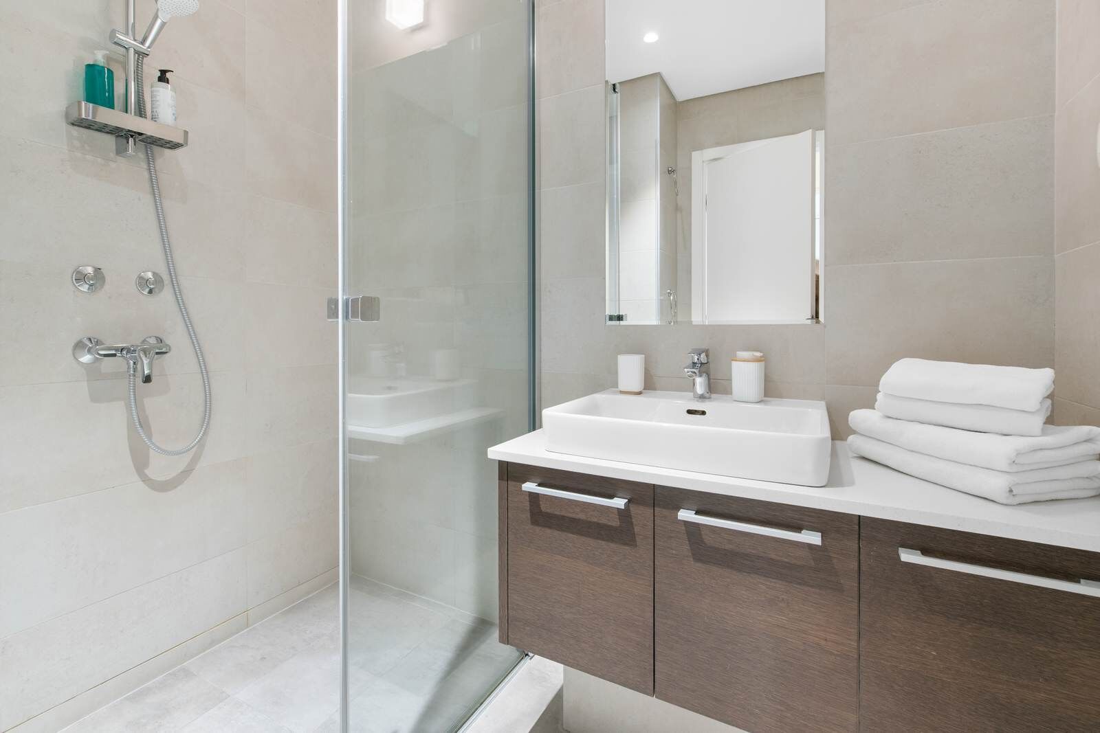 A modern bathroom with a glass shower enclosure, a white sink, and wooden cabinets.