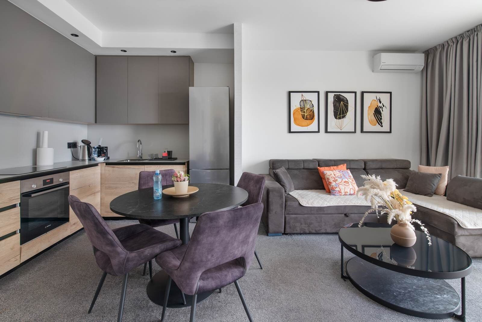 Un salon moderne avec un canapé gris, une table de salle à manger ronde et des chaises violettes.
