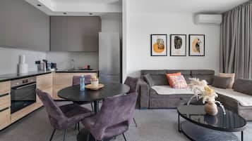A modern living room with a grey sofa, a round dining table, and purple chairs.