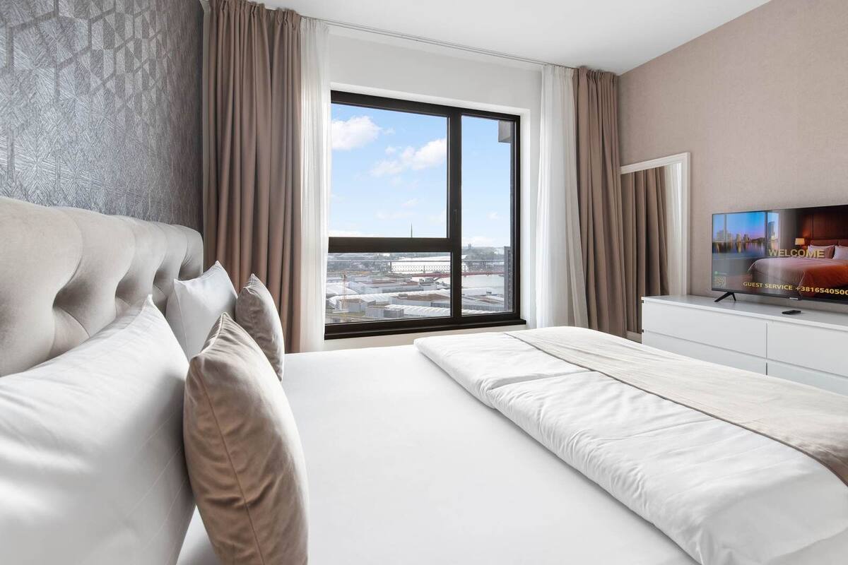 A hotel room with a large bed, a TV, and a window with a city view.