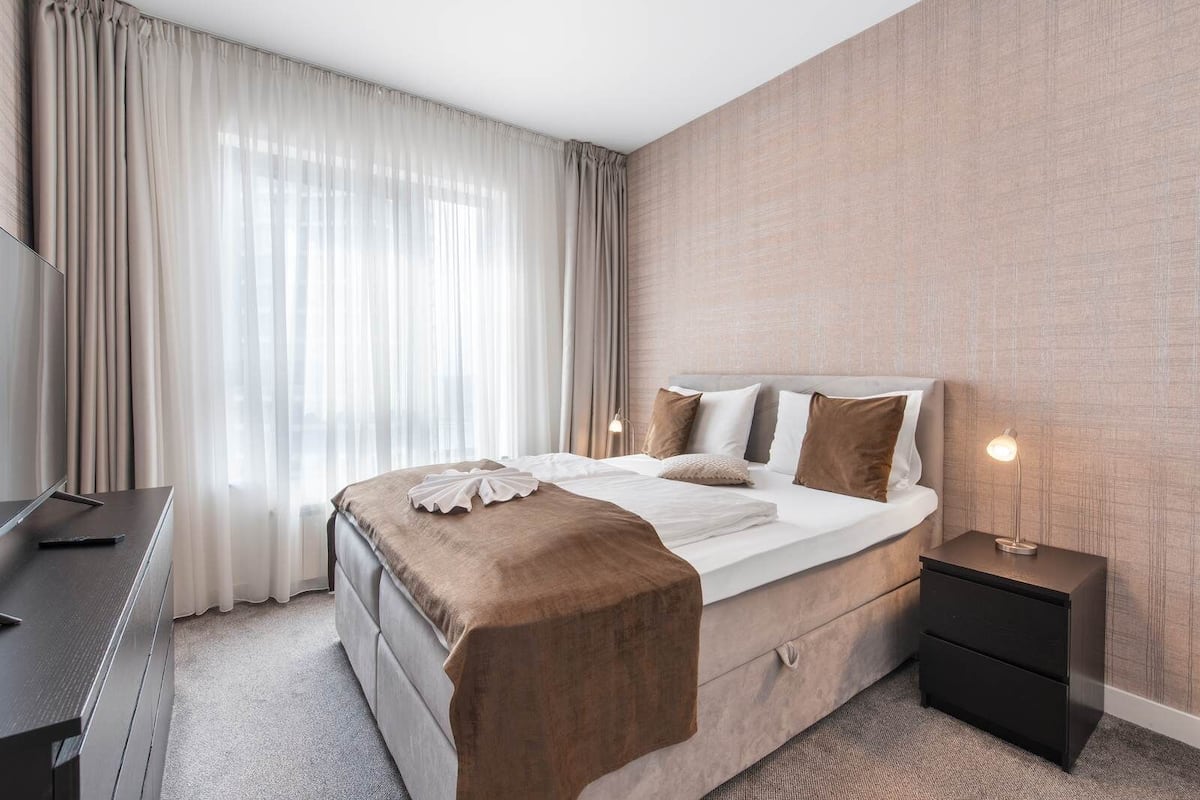 A hotel room with a bed, bedside table, lamp, and a TV.