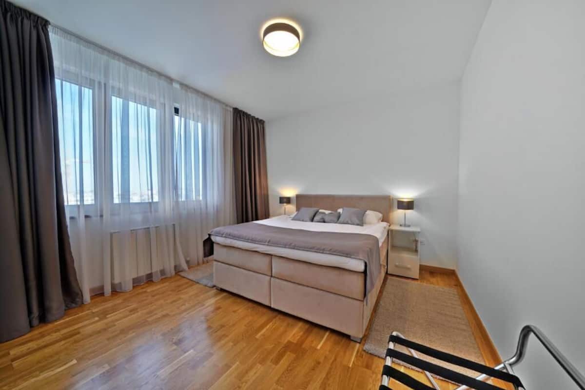A bedroom with a bed, bedside tables, a nightstand, and a window with curtains.