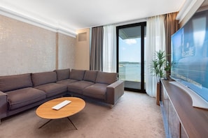 A modern hotel room with a sectional sofa, a small wooden coffee table, a flat-screen TV, and a balcony with a view of the water. - Belgrade Waterfront Riverside Apartments (Belgrade)