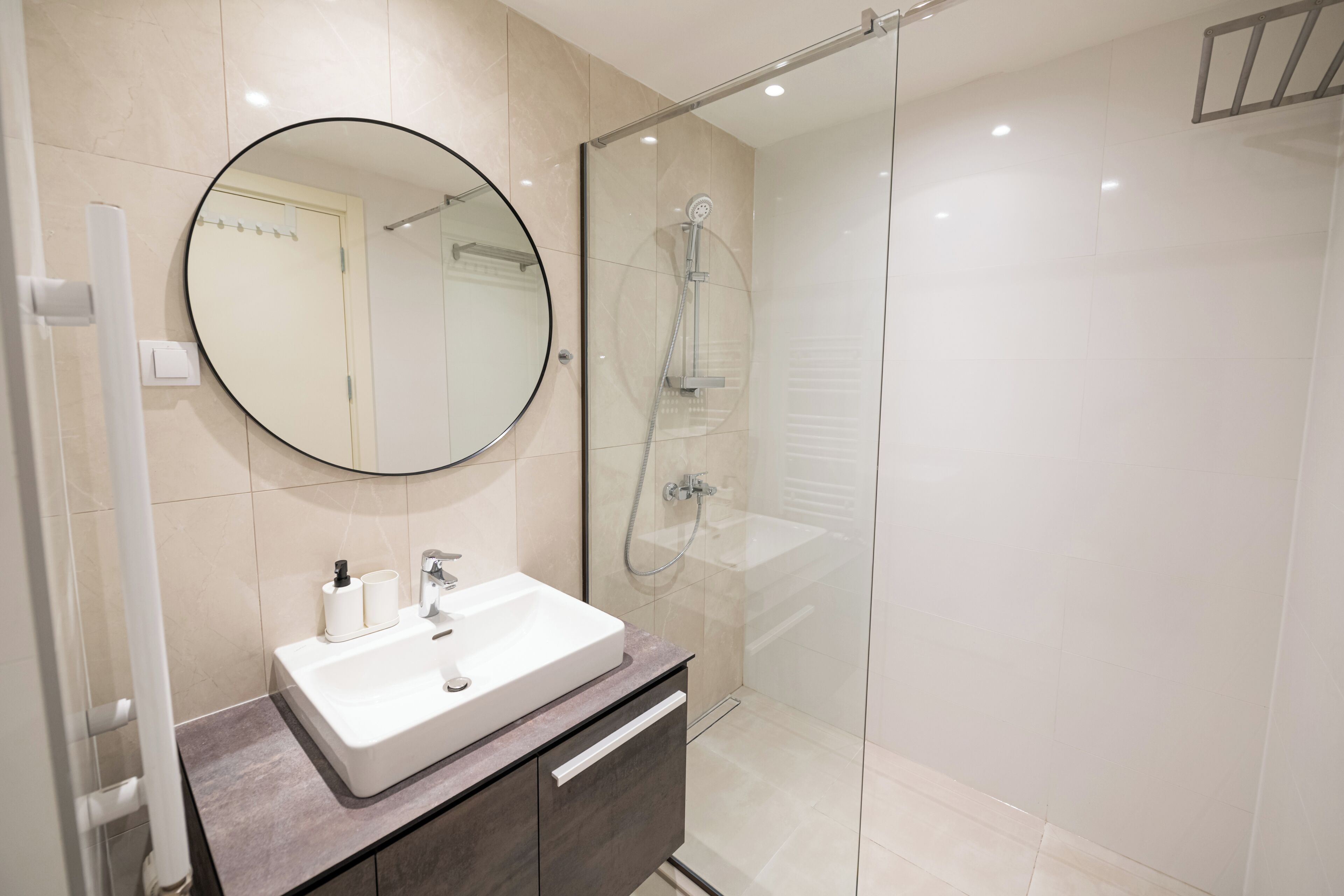 Un baño moderno con un lavabo blanco, mueble oscuro y zona de ducha con mampara de vidrio.