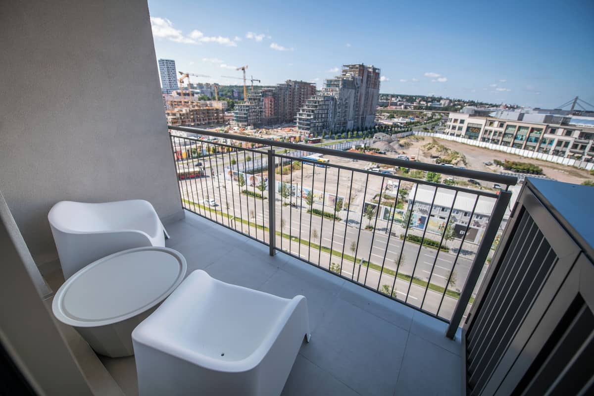 A balcony with two white chairs and a small table, overlooking a construction site and buildings.