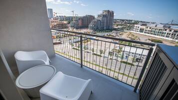 En balkon med to hvide stole og et lille bord, der ud til et byggeplads og bygninger.