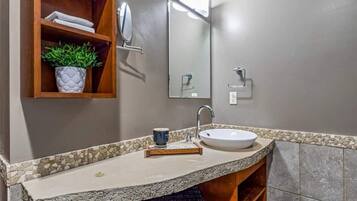 A bathroom with a granite countertop, a white sink, a mirror, and a shelf with a potted plant.