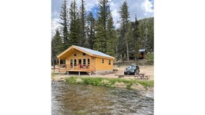 A wooden cabin with a porch, a small shed, and a car parked nearby. - 4K River Ranch • River Cabin 3 (sleeps 4) (Red River)