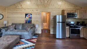 A cozy cabin interior with a living area featuring a sofa and a coffee table, a kitchen with modern appliances, and wooden walls. - 4K River Ranch • River Cabin 3 (sleeps 4) (Red River)