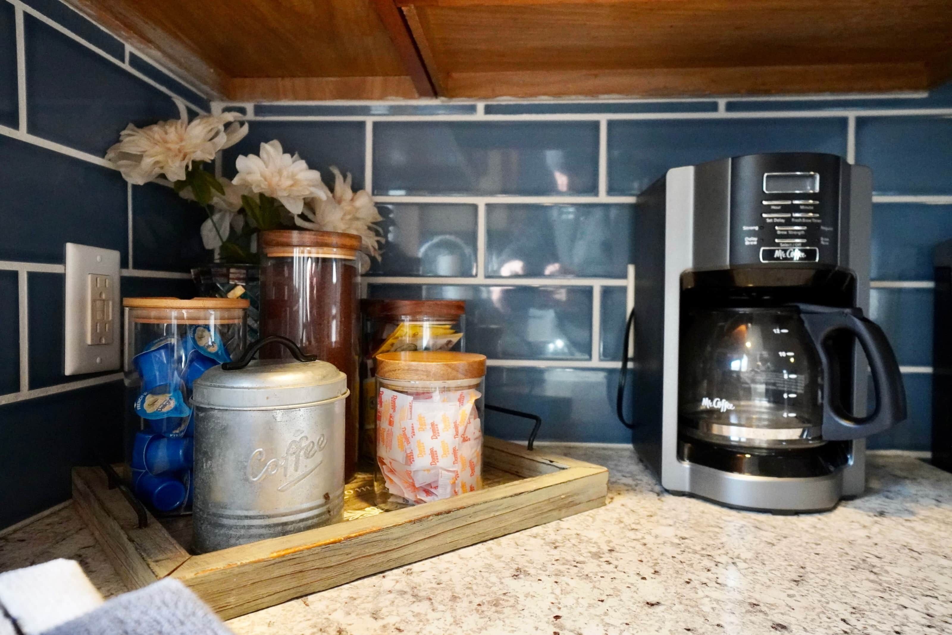 A kitchen counter with a coffee maker, jars, and a tray.