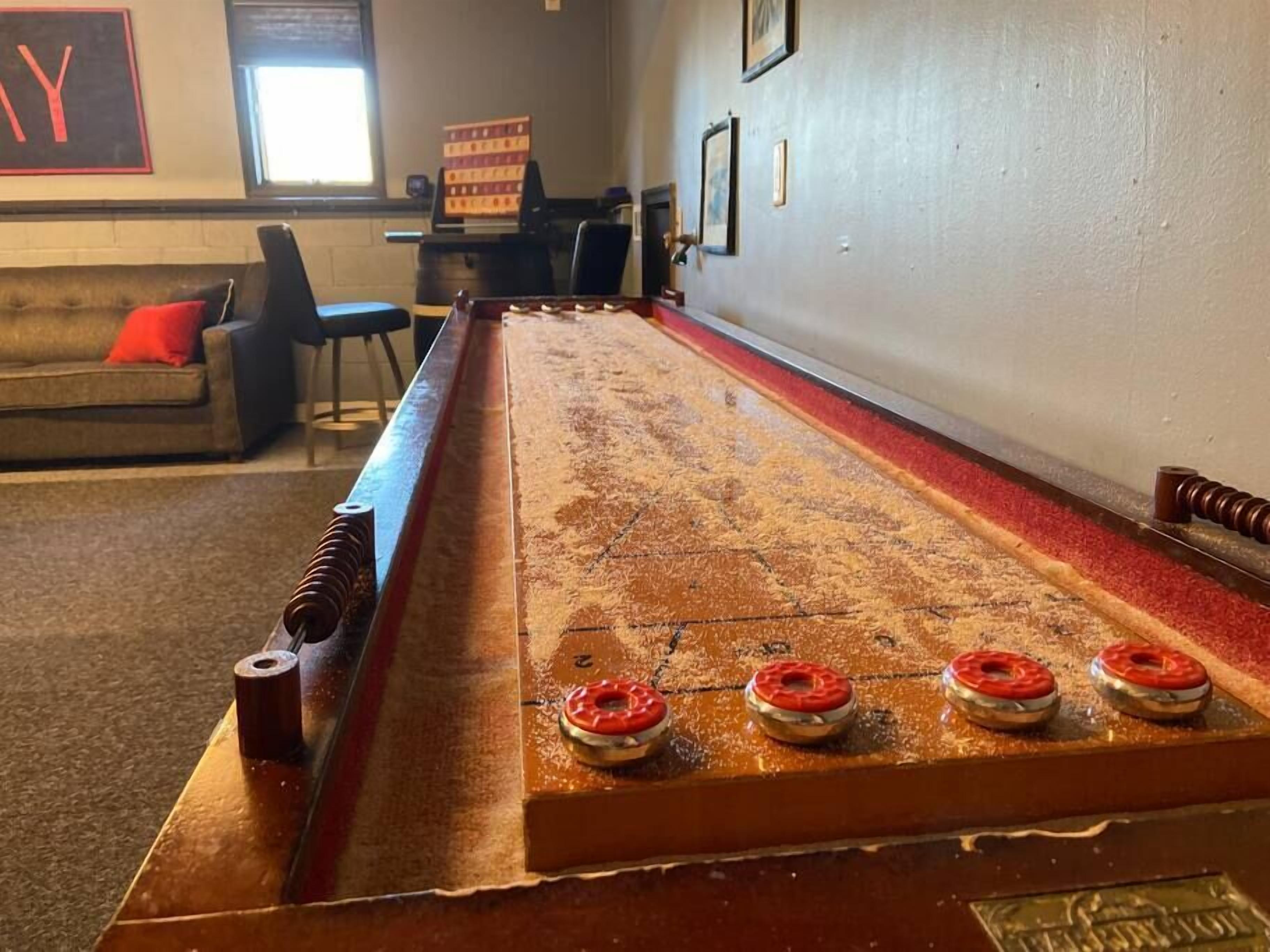 Ein Shuffleboard-Tisch mit vier roten und weißen Donuts darauf, ein roter Teppich und eine Couch mit einem roten Kissen im Hintergrund.