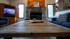 A living room with a stone fireplace, wooden ceiling, and a television on a wooden cabinet.