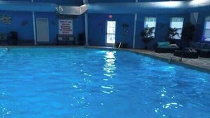 An indoor swimming pool with clear blue water, surrounded by walls and a ceiling with visible structural beams.