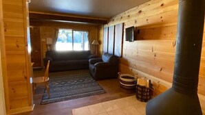 Interior acogedor de una cabaña con chimenea, un sofá, un sillón y una alfombra estampada.
