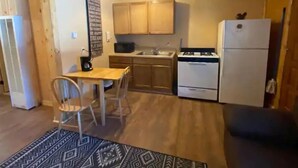 Cocina compacta con armarios de madera, estufa a gas, refrigerador y comedor con mesa y sillas.