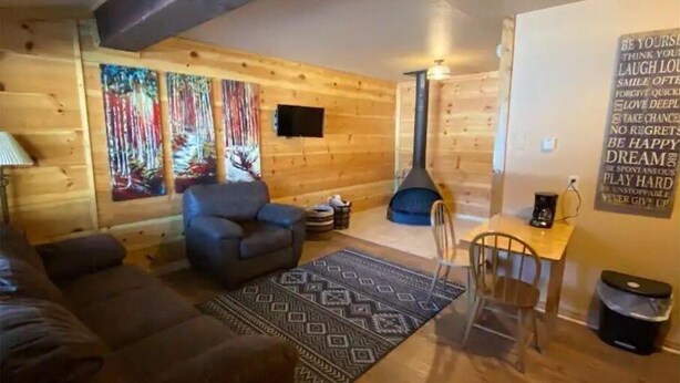 Un acogedor interior de cabaña de madera con un sofá, un sillón, una mesita y una chimenea.