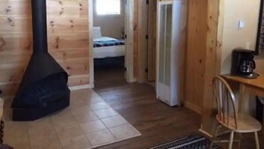 Una cabaña acogedora con estufa de leña, una cama, refrigerador y comedor.