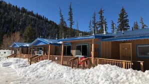Una fila de cabañas con fachada de madera y techos azules, rodeadas de nieve y árboles.