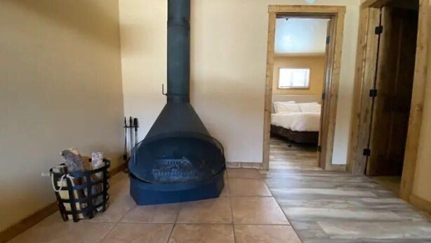 A room with a large black wood stove, a wooden door, and a bed with white bedding. - 4K River Ranch • Condo 3 (sleeps 4) (Red River)
