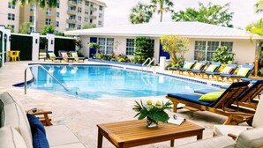 A poolside area with lounge chairs and a wooden table, surrounded by a building with large windows and a covered patio. - Casa Cordova by Lowkl (Fort Lauderdale)