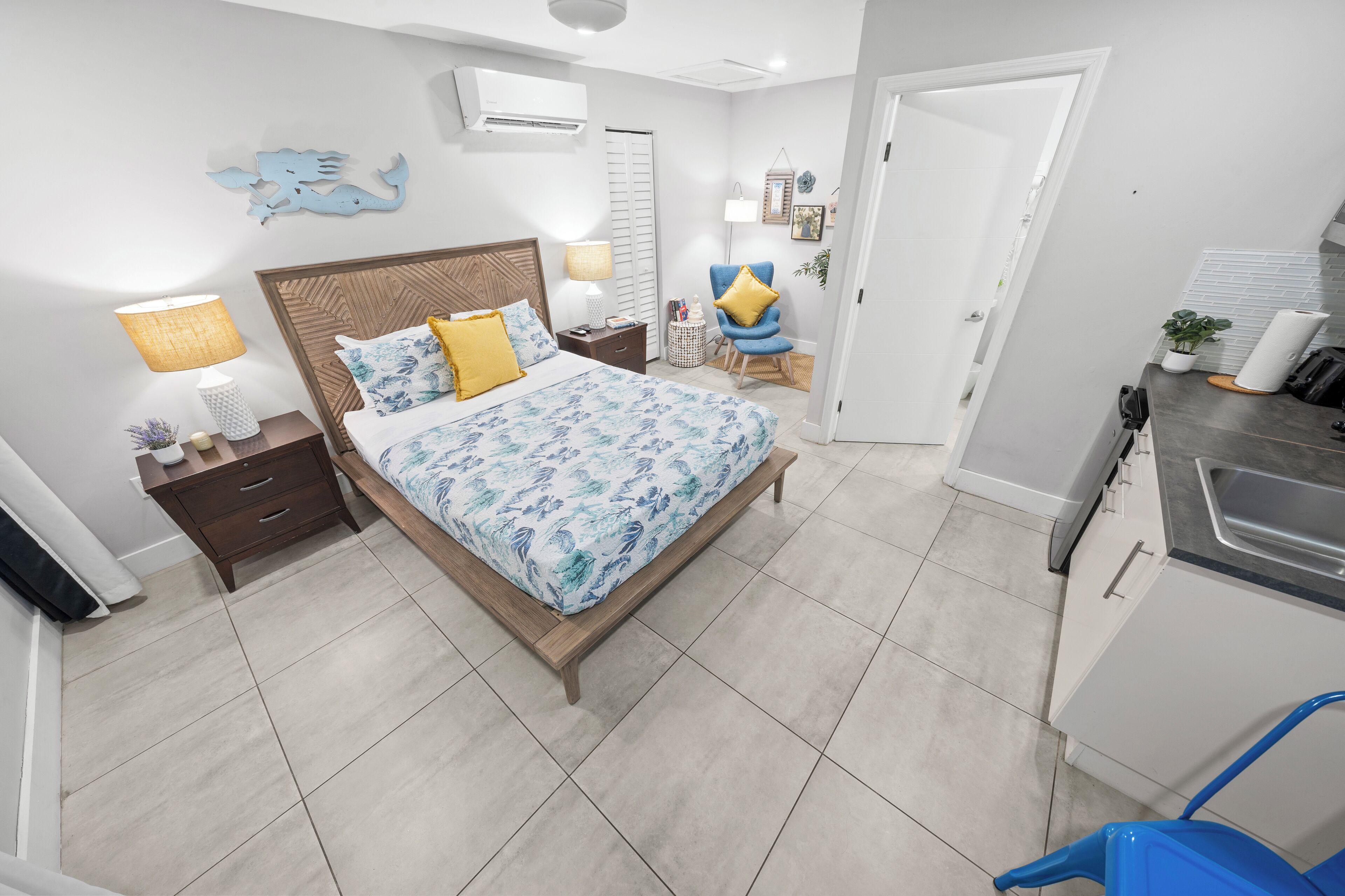 Un dormitorio con cama, mesitas de noche, lámpara, silla y una pequeña mesa.