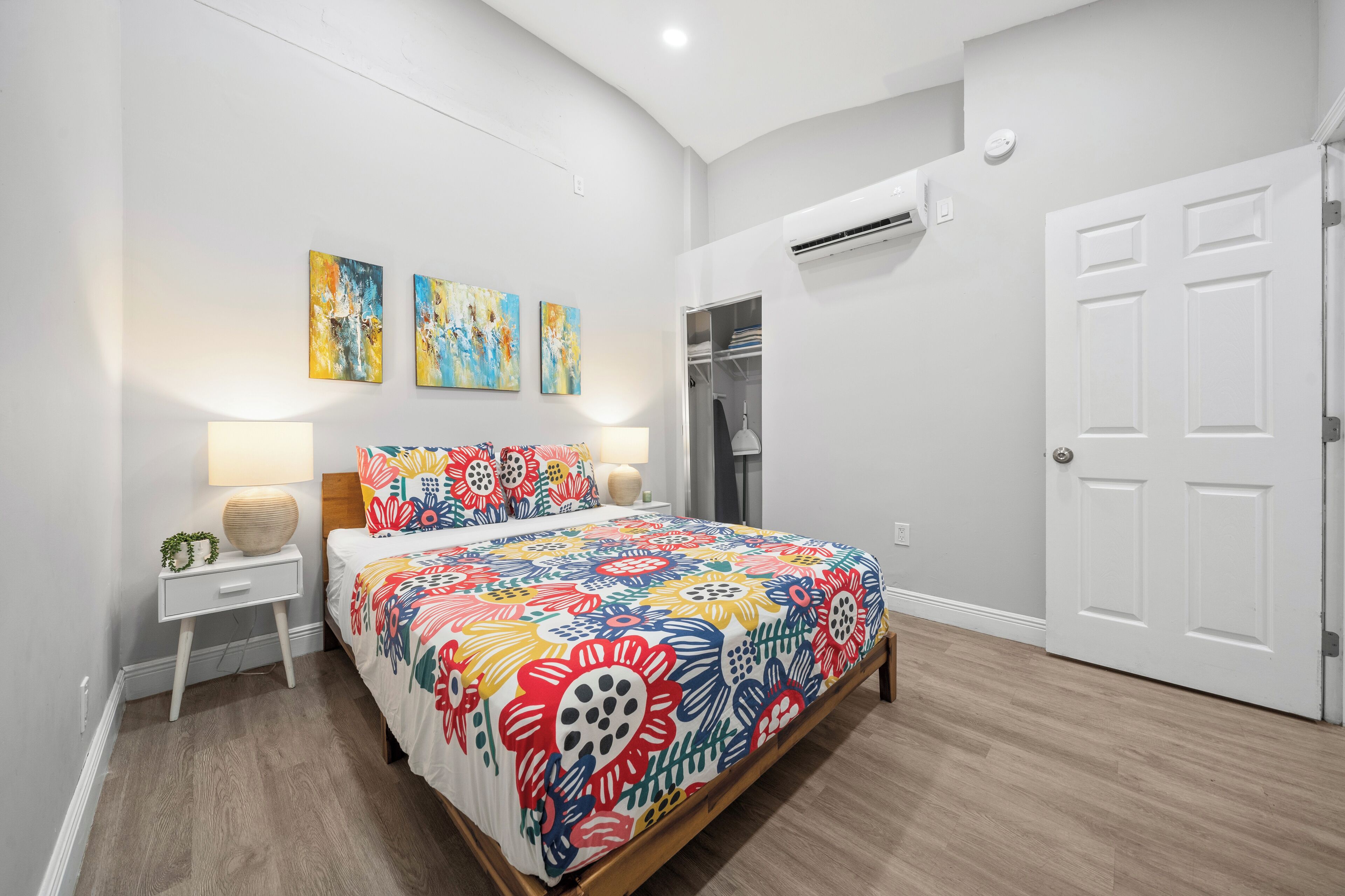 A bedroom with a bed, bedside table, wall art, and a closet.