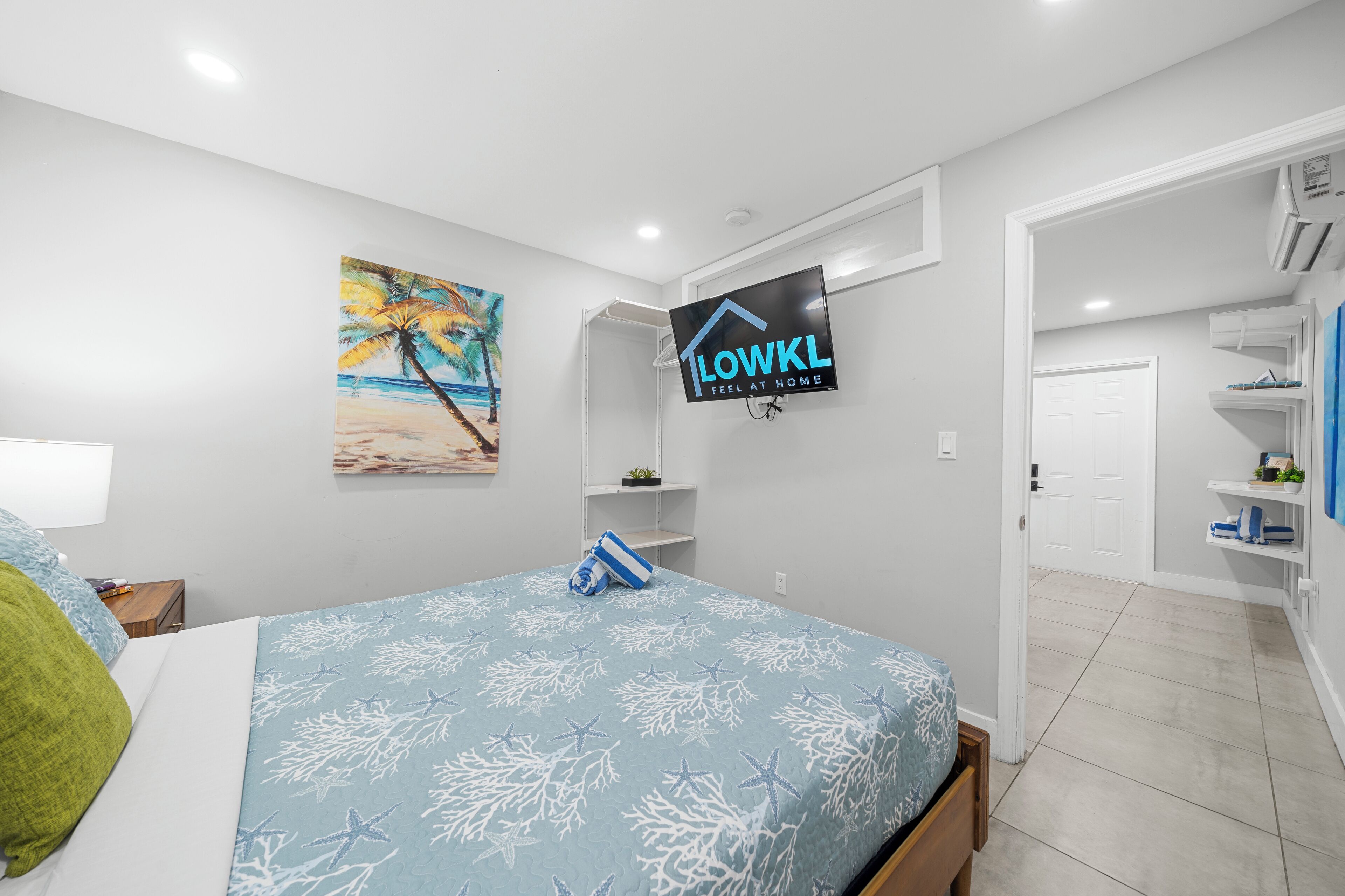 A bedroom with a bed, a painting, a TV, and a door leading to another room.