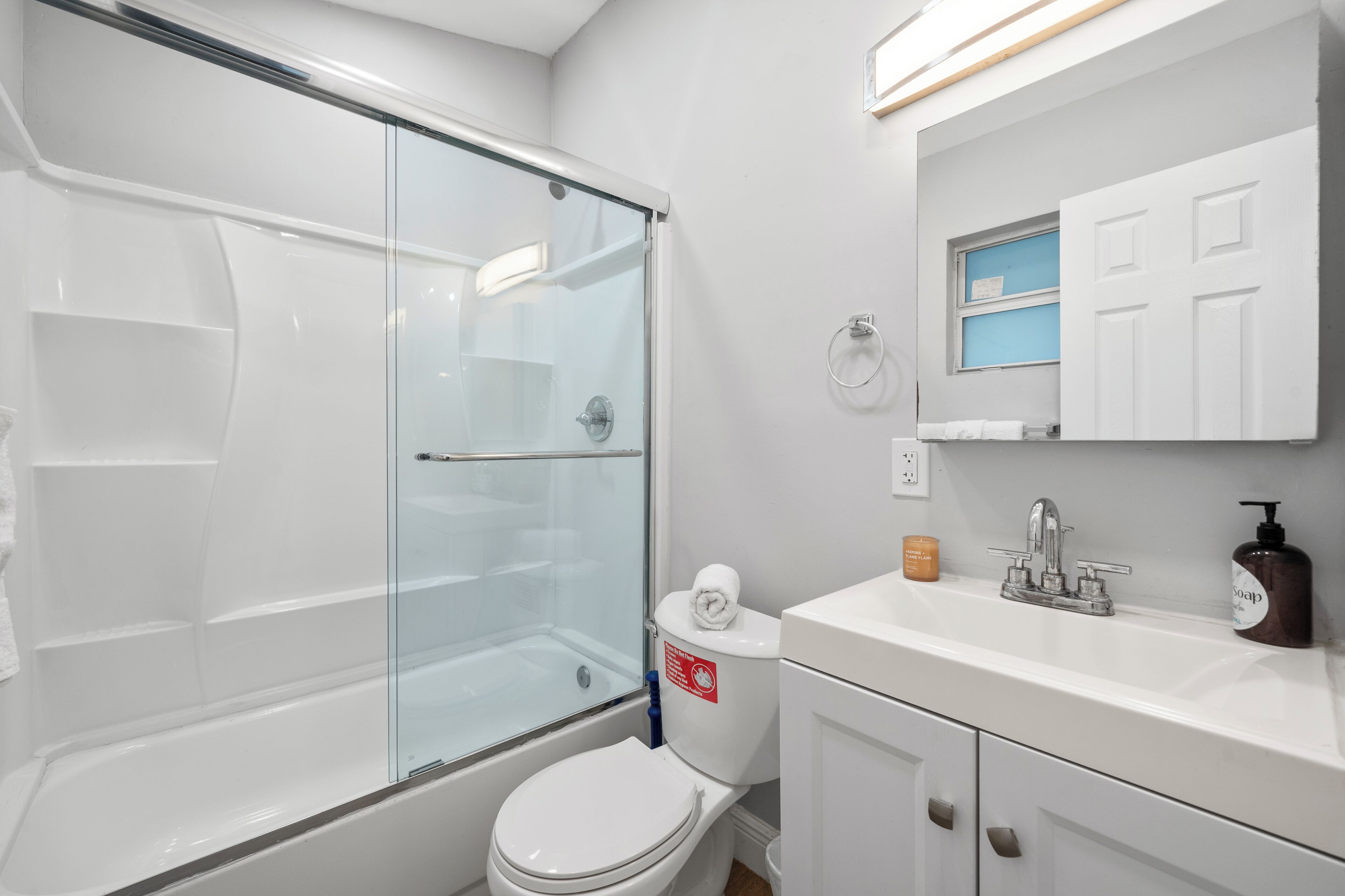 A modern bathroom with a glass shower enclosure, a white toilet, and a sink with a soap dispenser.