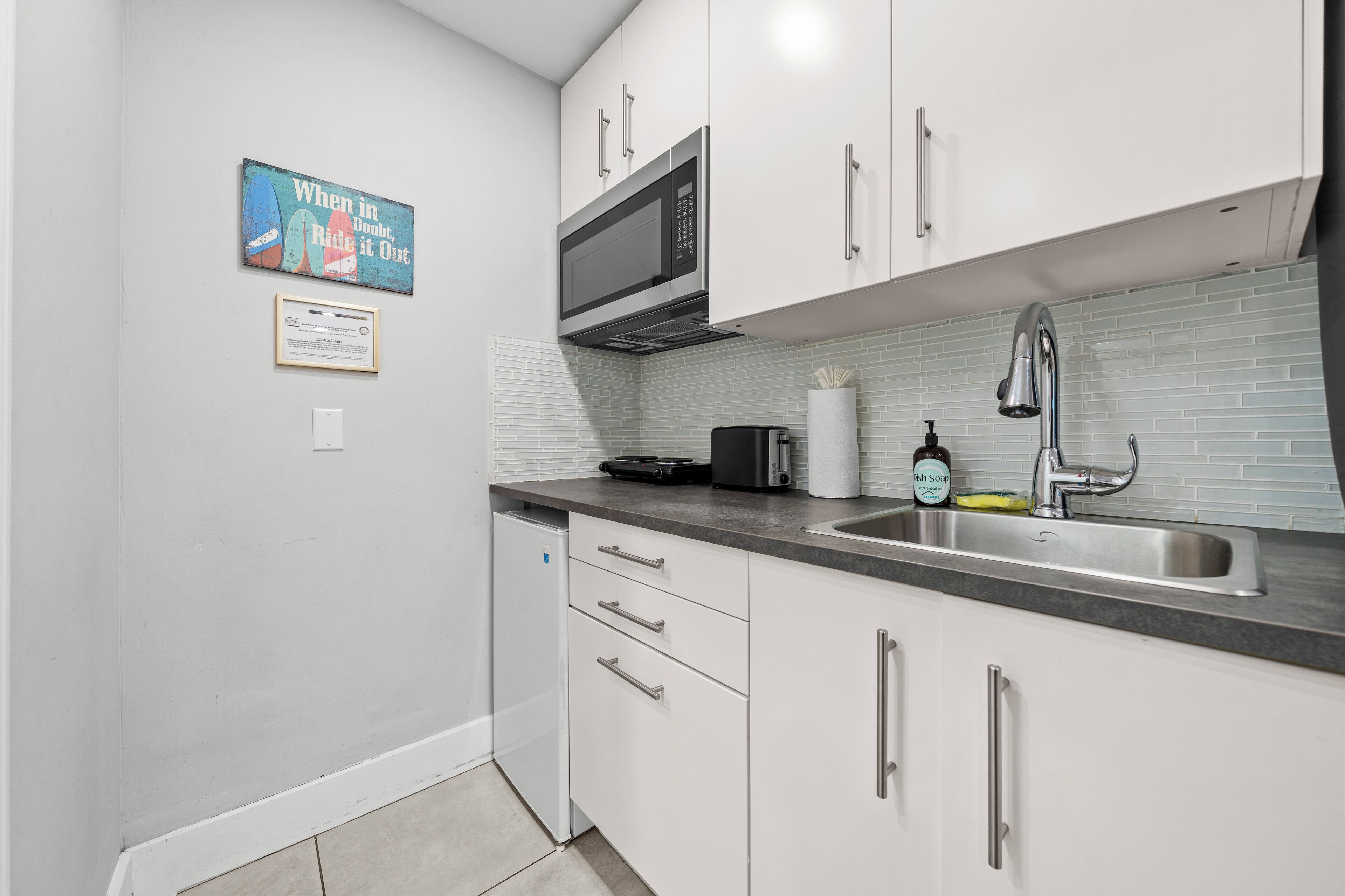 A modern kitchen with white cabinets, a stainless steel sink, a microwave, and a toaster.
