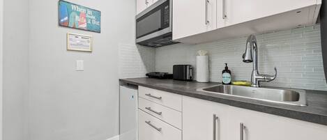 A modern kitchen with white cabinets, a stainless steel sink, a microwave, and a toaster.