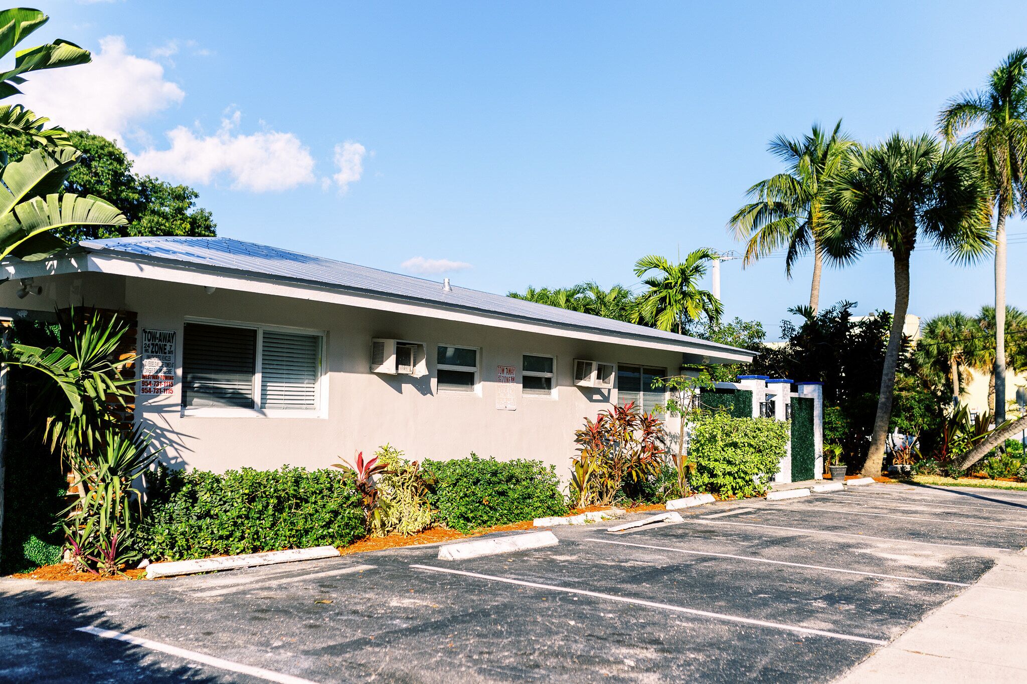 Un motel de una sola planta con estacionamiento, rodeado de vegetación tropical y palmeras.