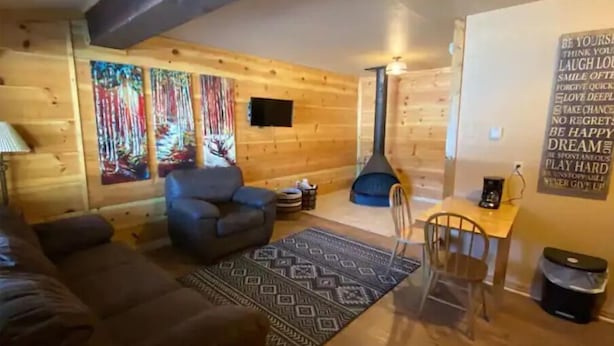 L’intérieur d’un chalet confortable, avec un canapé, un fauteuil, une petite table, un tapis décoratif et un mur orné de citations inspirantes.