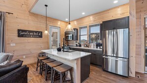 A modern kitchen with wooden walls, a central island, bar stools, and stainless steel appliances. - NEW Luxury Cabin, Lake and Mountain Views/ Easy Access to Pigeon Forge! (Sevierville)