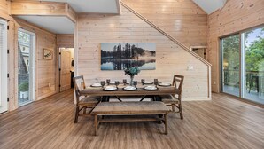 A wooden interior with a dining area featuring a large table set for six, a bench, and a staircase. - NEW Luxury Cabin, Lake and Mountain Views/ Easy Access to Pigeon Forge! (Sevierville)