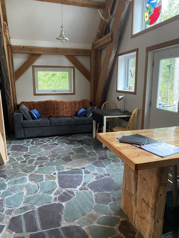 A cozy room with a stone floor, a wooden ceiling, a sofa with cushions, a table with a laptop, and windows with natural light. - Hummingbird Haven Charming Cabin in the Mountains (Golden)
