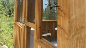 Una cabaña de madera con ventanas amplias, una escultura de pájaro metálico y vistas a árboles.