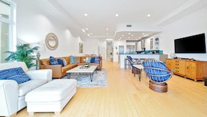 A modern living room with a sofa, coffee table, and a unique blue chair. A kitchen area is visible in the background. - Ultimate Paradise Retreat  (Oceanside)