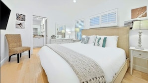 A bedroom with a large bed, a chair, a dresser, and a nightstand. - Ultimate Paradise Retreat  (Oceanside)