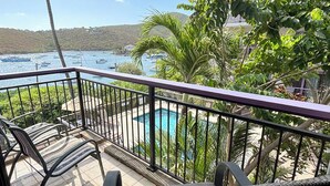 A balcony with a view of a swimming pool, surrounded by greenery and a hilly landscape. - This exceptional property offers the convenience of being just a short stroll from Cruz Bay, all while providing the comfort of full air conditioning. Don't miss out on this perfect blend of location and luxury! (St John)