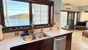 A kitchen with a large window, a sink, and a view of boats on the water. - This exceptional property offers the convenience of being just a short stroll from Cruz Bay, all while providing the comfort of full air conditioning. Don't miss out on this perfect blend of location and luxury! (St John)