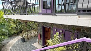 A multi-level building with a stone facade, a purple door labeled 'laundry,' and a balcony with a railing. - This exceptional property offers the convenience of being just a short stroll from Cruz Bay, all while providing the comfort of full air conditioning. Don't miss out on this perfect blend of location and luxury! (St John)